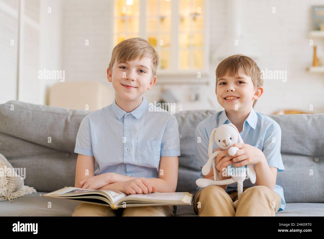 Teach your child to read book as teenager. Caucasian child looking into book while studying with teenager on couch in living room at home. Elder brother is reading book in living room on sofa brother Stock Photo