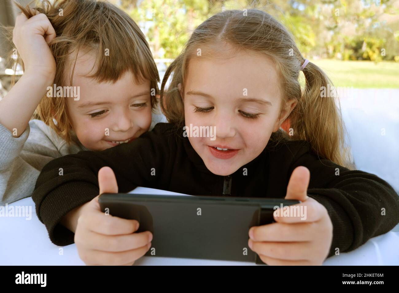 Little boy and girl pretty siblings using smart phone playing videogames, watch cartoons discuss new cool funny mobile application, having fun on week Stock Photo