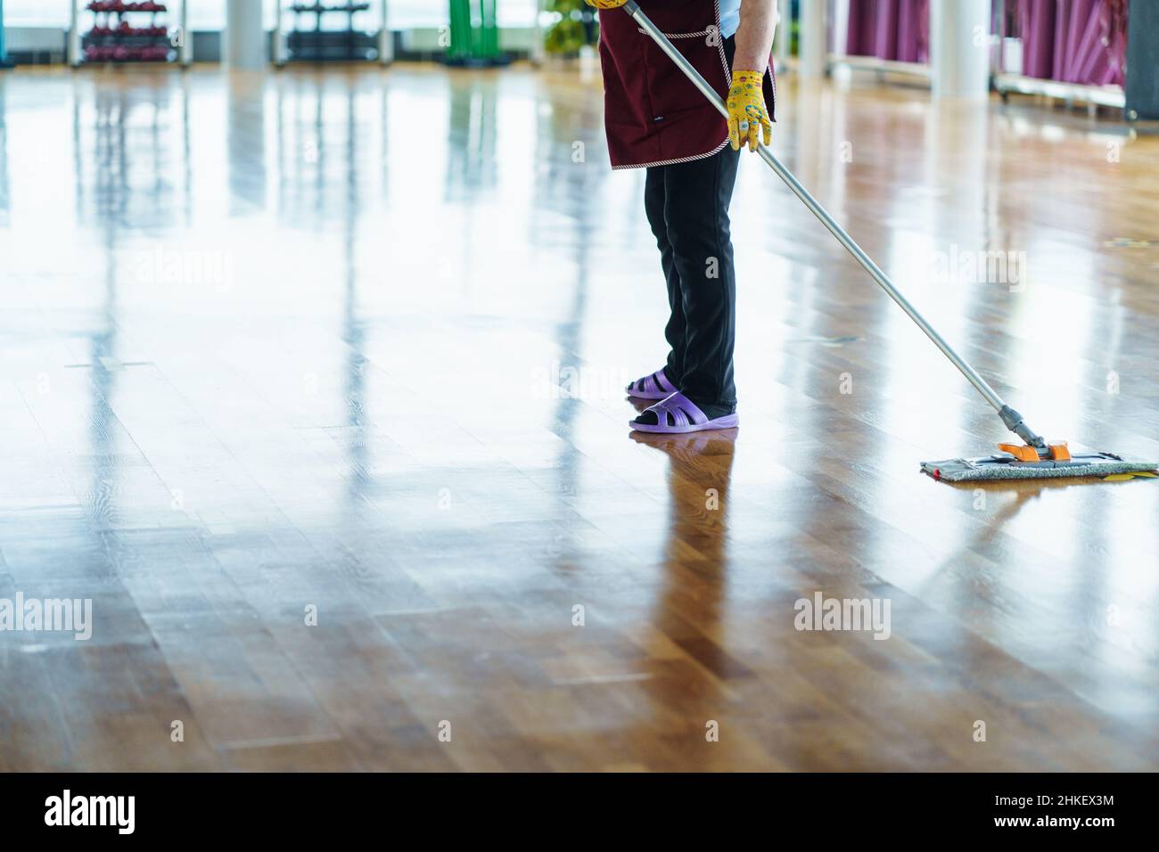 Unrecognizable cleaning woman in red uniform, black jeans, yellow rubber gloves and purple rubber slippers mopping floor Stock Photo