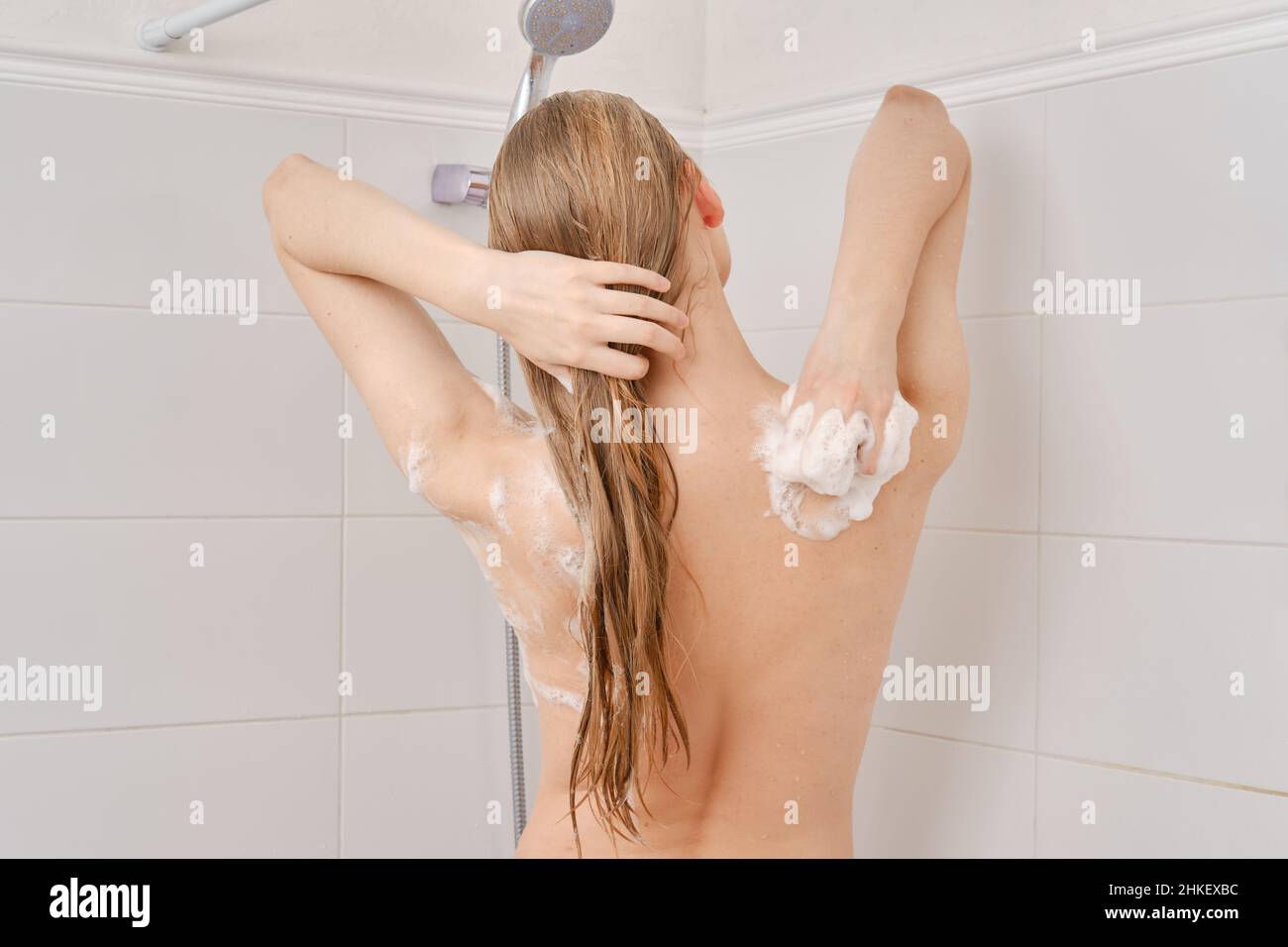 Young woman soaps her body in bathroom while turning back to camera Stock Photo