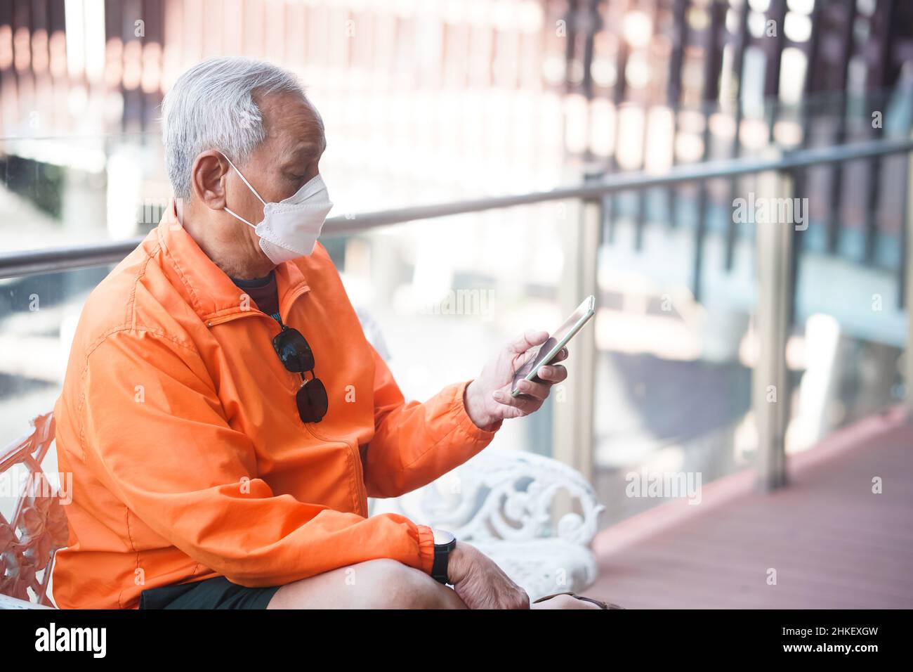 asian old elder senior man elderly wearing mask using mobile smart phone cellphone outdoor. mature retirement lifestyle Stock Photo