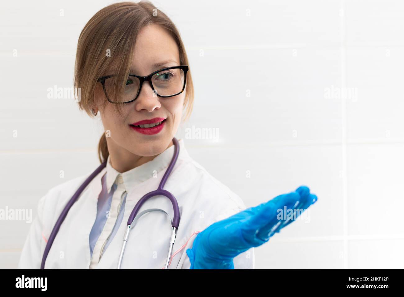 Beautiful young happy doctor woman in medical gloves and glasses with a stethoscope in the hospital shows hand gestures. Selective focus. Portrait. Cl Stock Photo