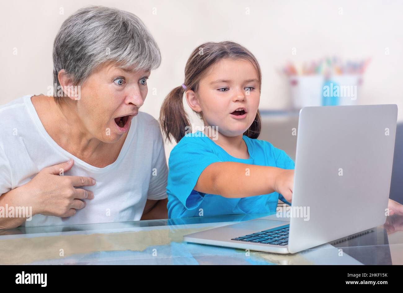 A child and a senior look at a laptop with delight and surprise Stock Photo