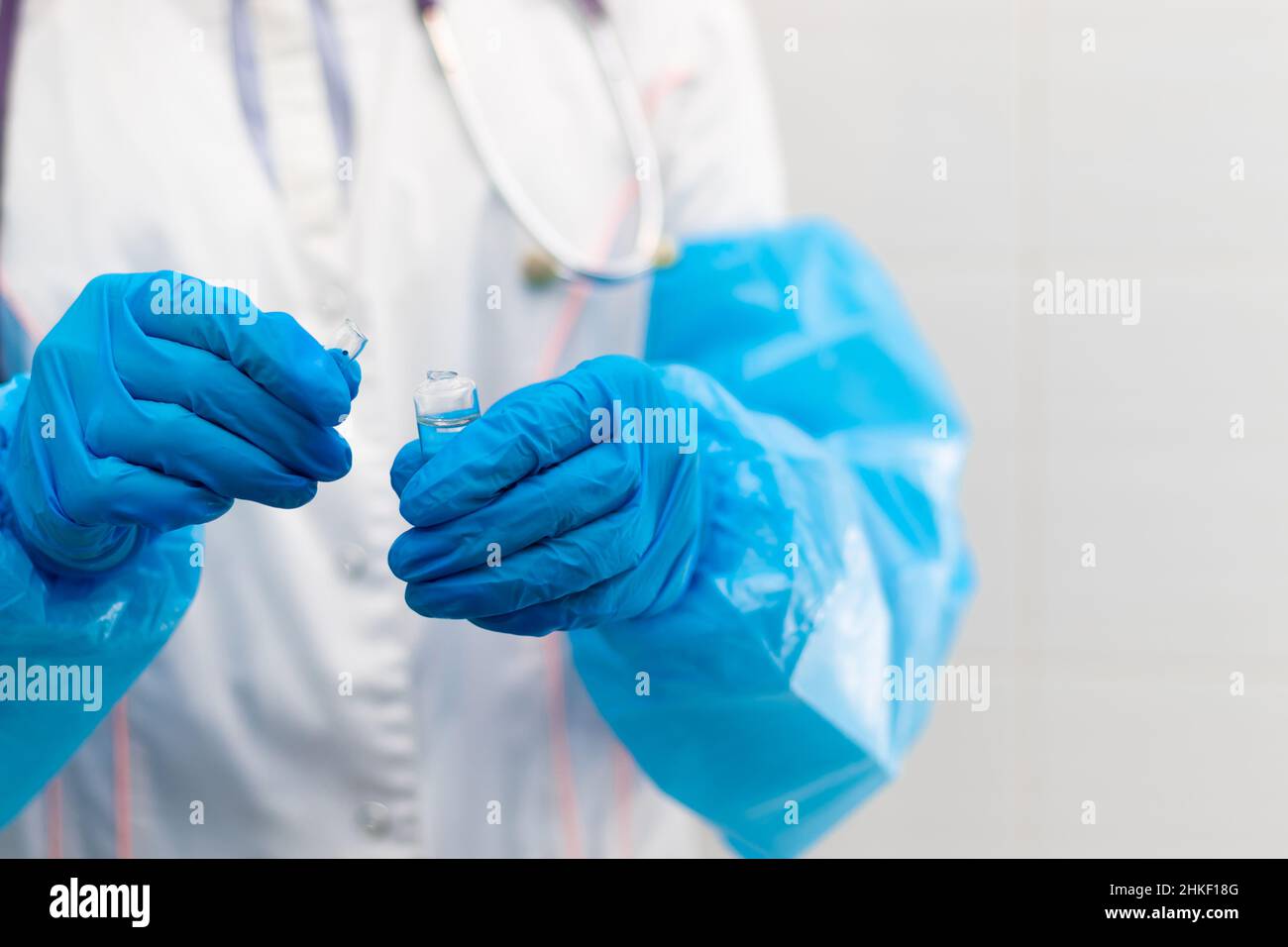 Doctor's hands in rubber medical gloves hold an ampoule of medicine in a hospital during the coronavirus pandemic. Selective focus. Close-up Stock Photo