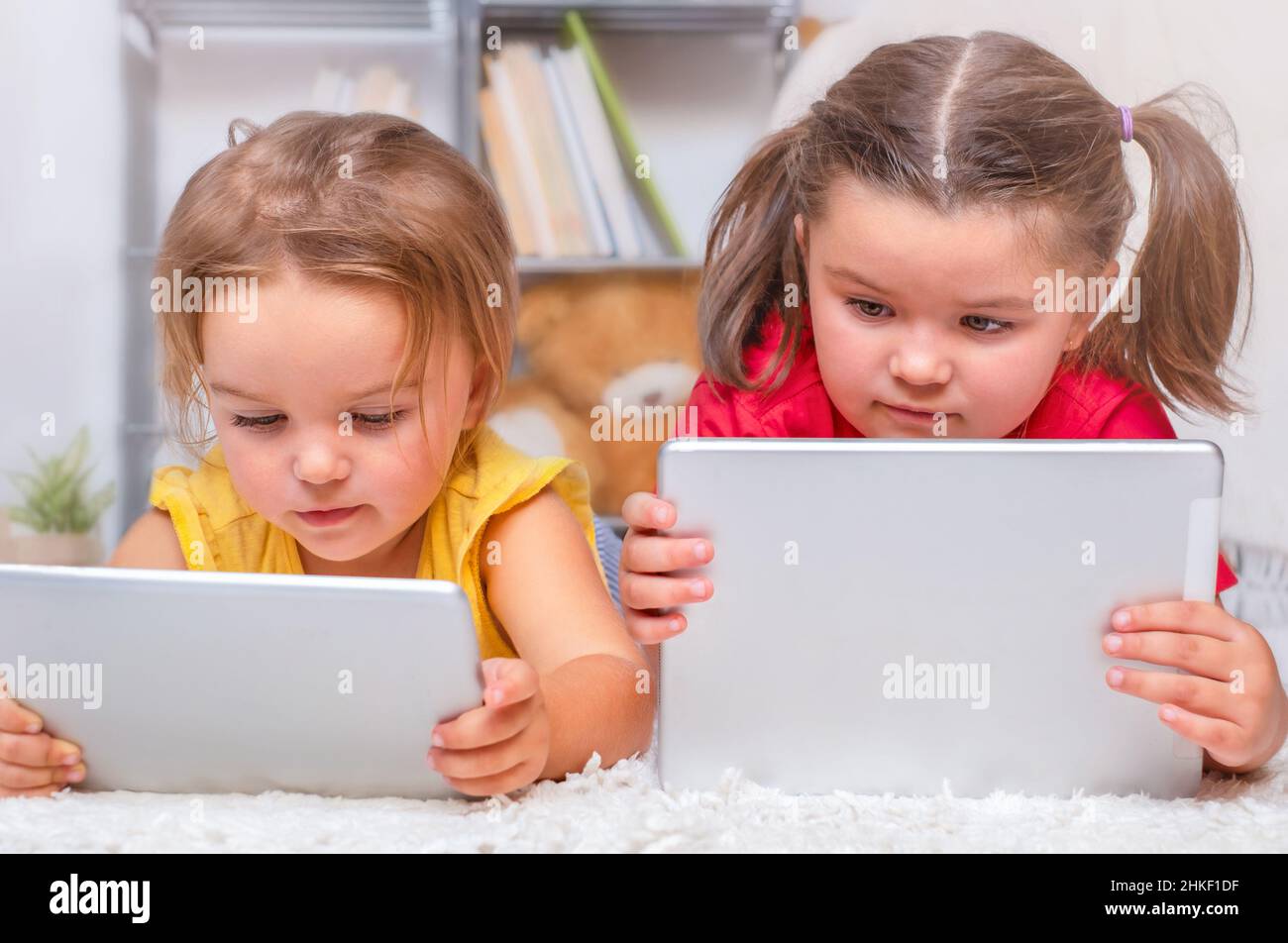 Two children lie on the floor and carefully look at the tablets Stock
