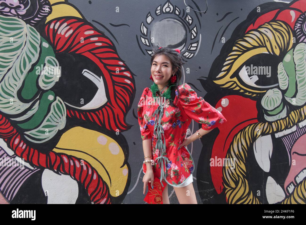 Young Thai Woman wears a traditional Chinese dress (cheongsam) and smiles for the camera  in front of a mural, Chinatown, Bangkok, Thailand Stock Photo