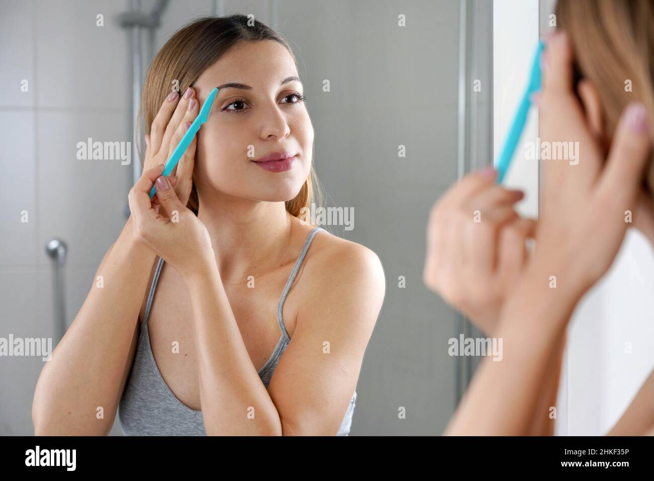 Facial hair removal. Beautiful young woman shaving her face by razor at