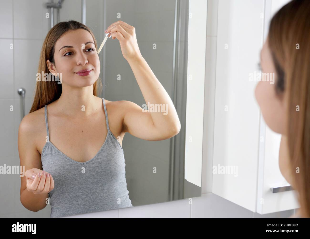 Young Skin Care Routine. Beautiful girl applying a Vitamin C booster antioxidant ascorbic acid anti aging serum to her face while holding a pipette in Stock Photo