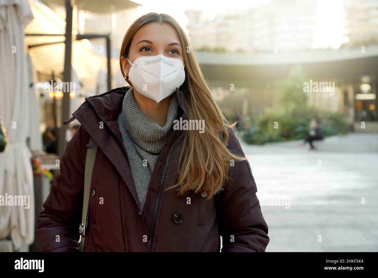 Happy young woman using medical face mask over city background looking to the side and staring away thinking Stock Photo