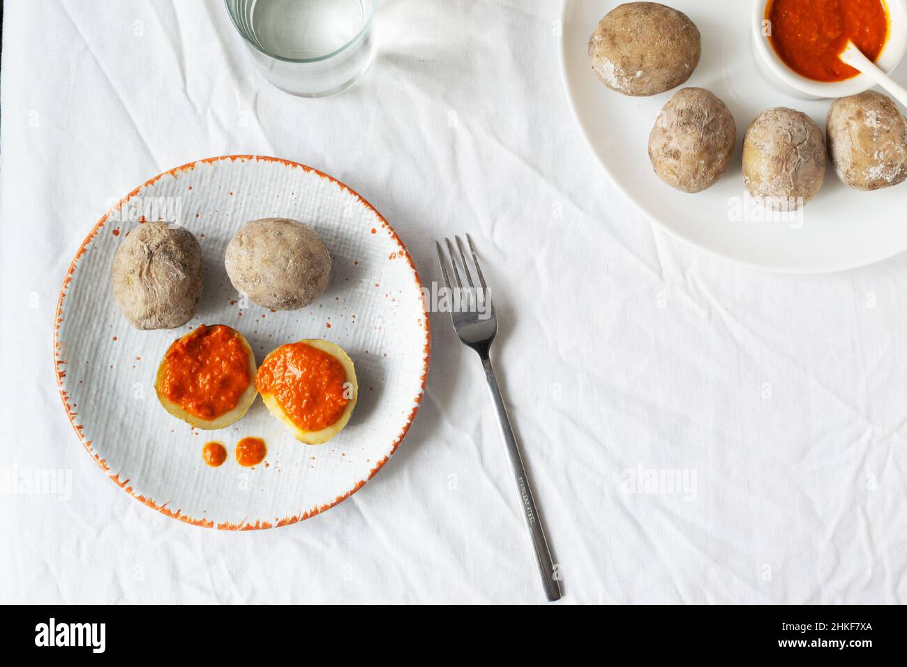 Potatoes on a white plate with red sauce with a fork on a white tablecloth. A traditional Canarian dish is papas arrugadas. Vegetables are boiled in w Stock Photo