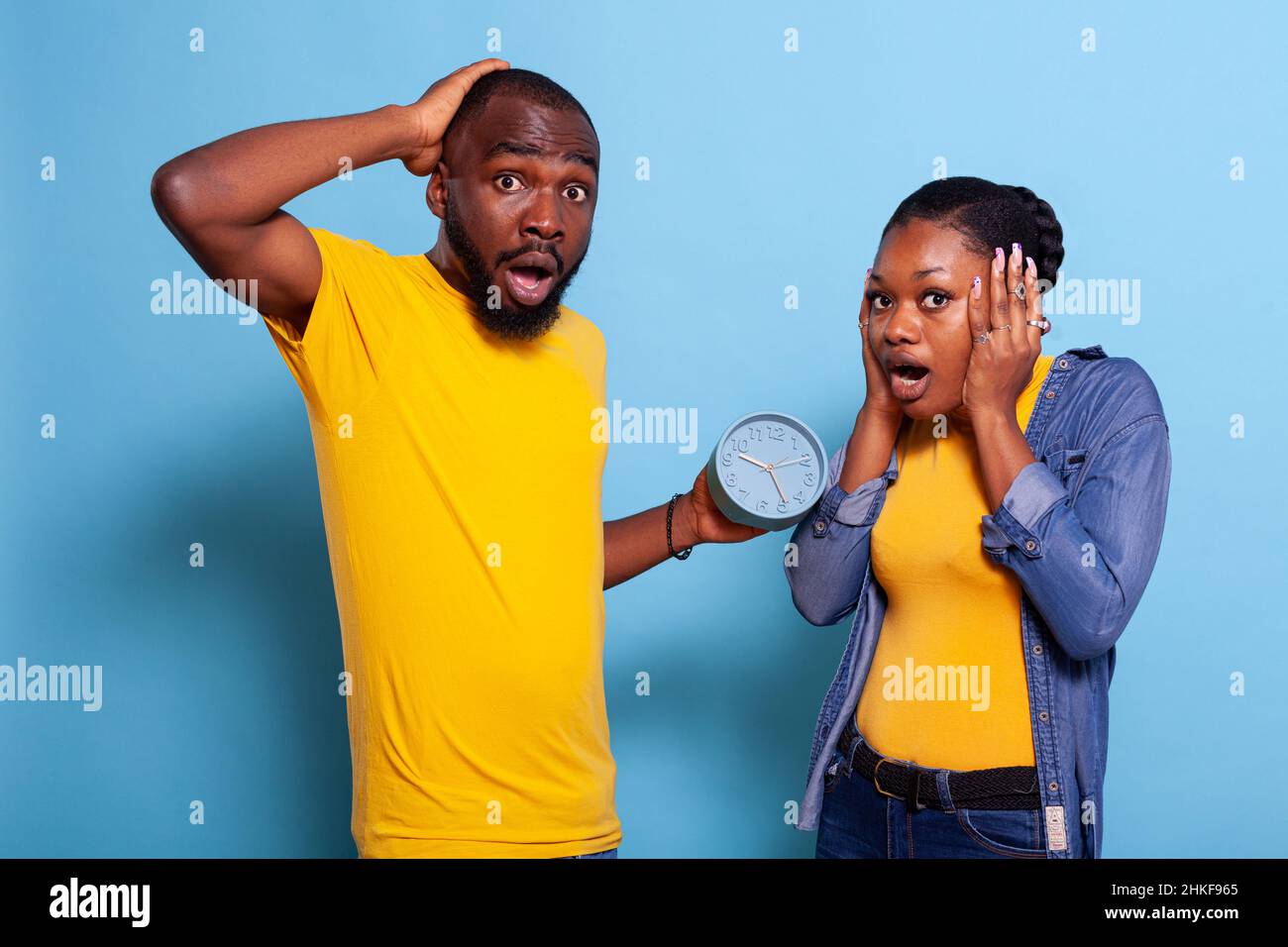 Shocked man and woman looking at time on clock and running late to work schedule. Impatient couple checking hour and minutes on watch, being in panic about deadline. Stressed people Stock Photo