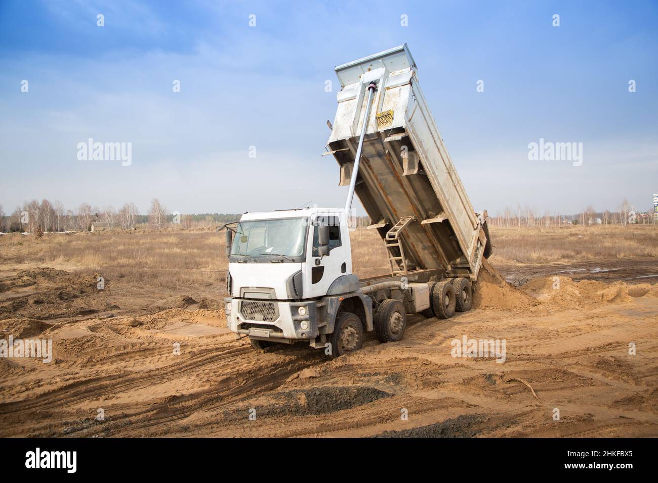 dump truck with a raised body in the process of working on a construction site. transportation and unloading of soil on a construction vehicle. Stock Photo