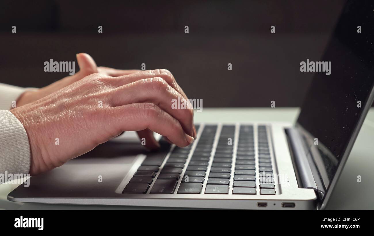 Elderly woman works at laptop typing quickly on keyboard Stock Photo