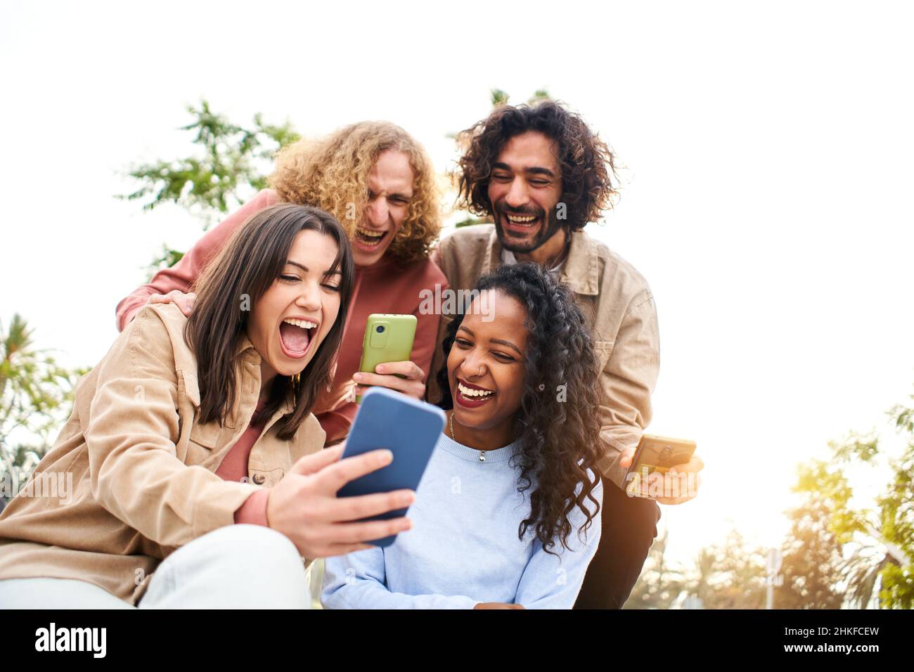 Happy friends watching screen mobile phone with a surprised face and smiling. Young adult people using smartphone and having fun. Stock Photo