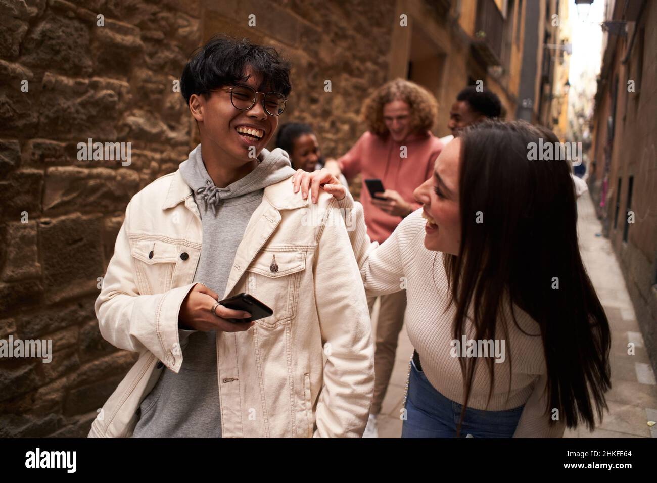 Group of happy friends using phone outdoors while walking and laughing. Stock Photo