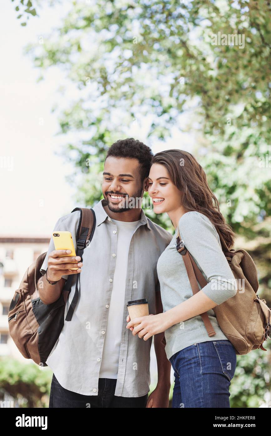Young couple using smartphone outdoors. Joyful smiling woman and man looking at mobile phone in a city. Stock Photo