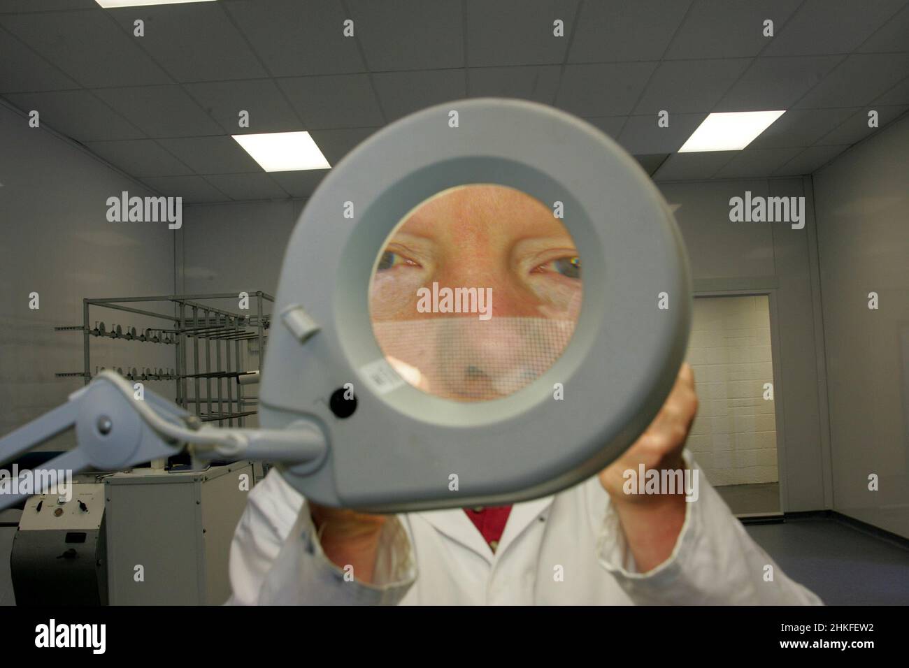 Technician in laboratory using a large illuminated magnifying glass to view electrical component and circuit boards. Stock Photo