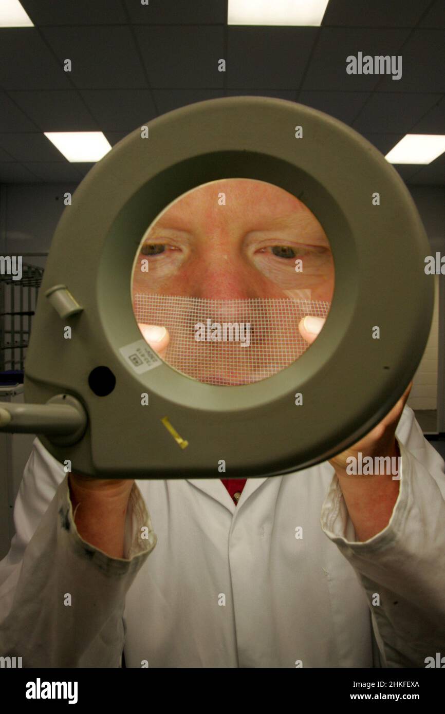 Technician in laboratory using a large illuminated magnifying glass to view electrical component and circuit boards. Stock Photo