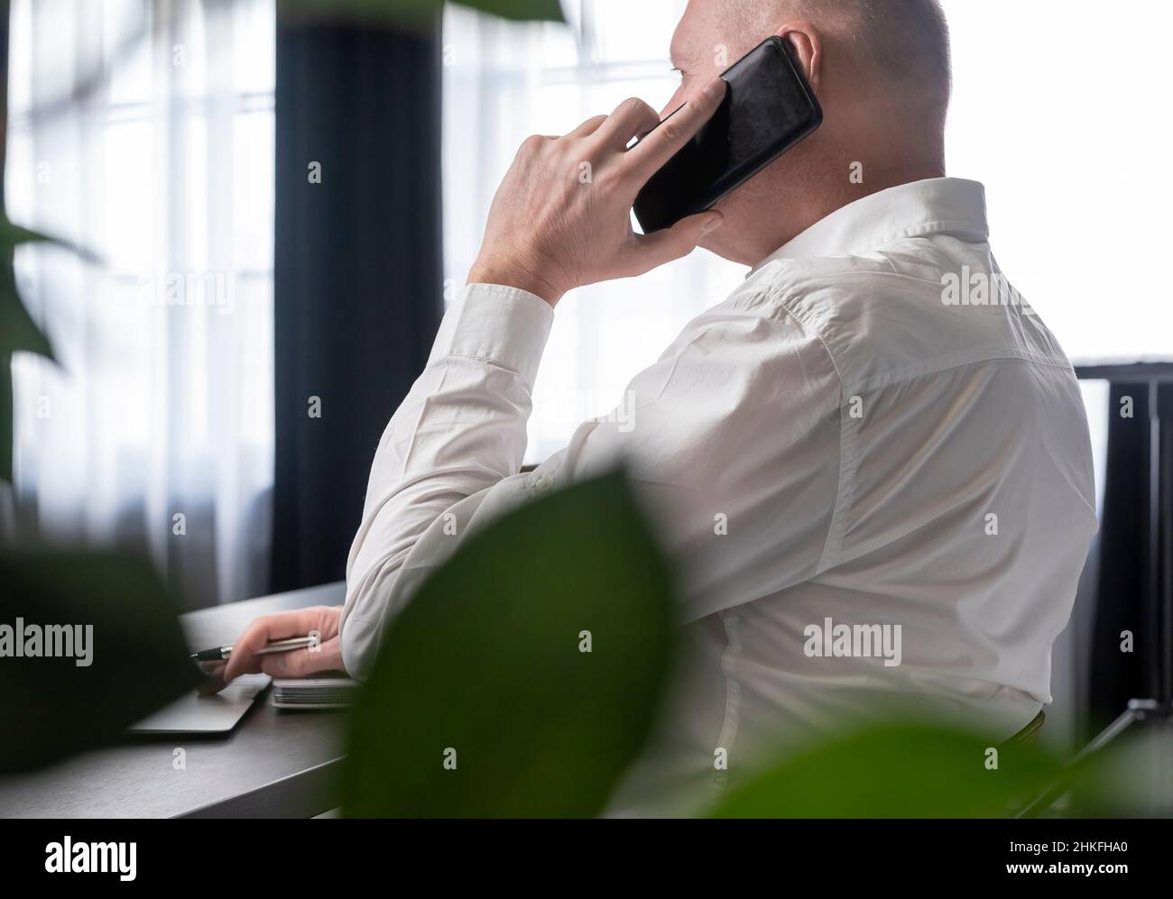 Mature businessman sitting at desk with laptop and planner. Employee working in office and answering phone call. Business call concept. High quality photo Stock Photo