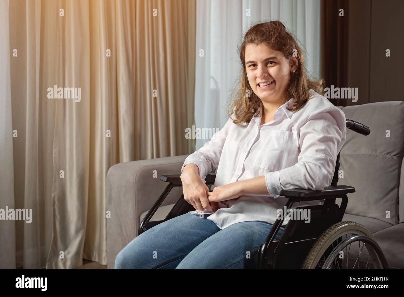 Disabled woman smiles sitting in wheelchair by sofa at home Stock Photo ...