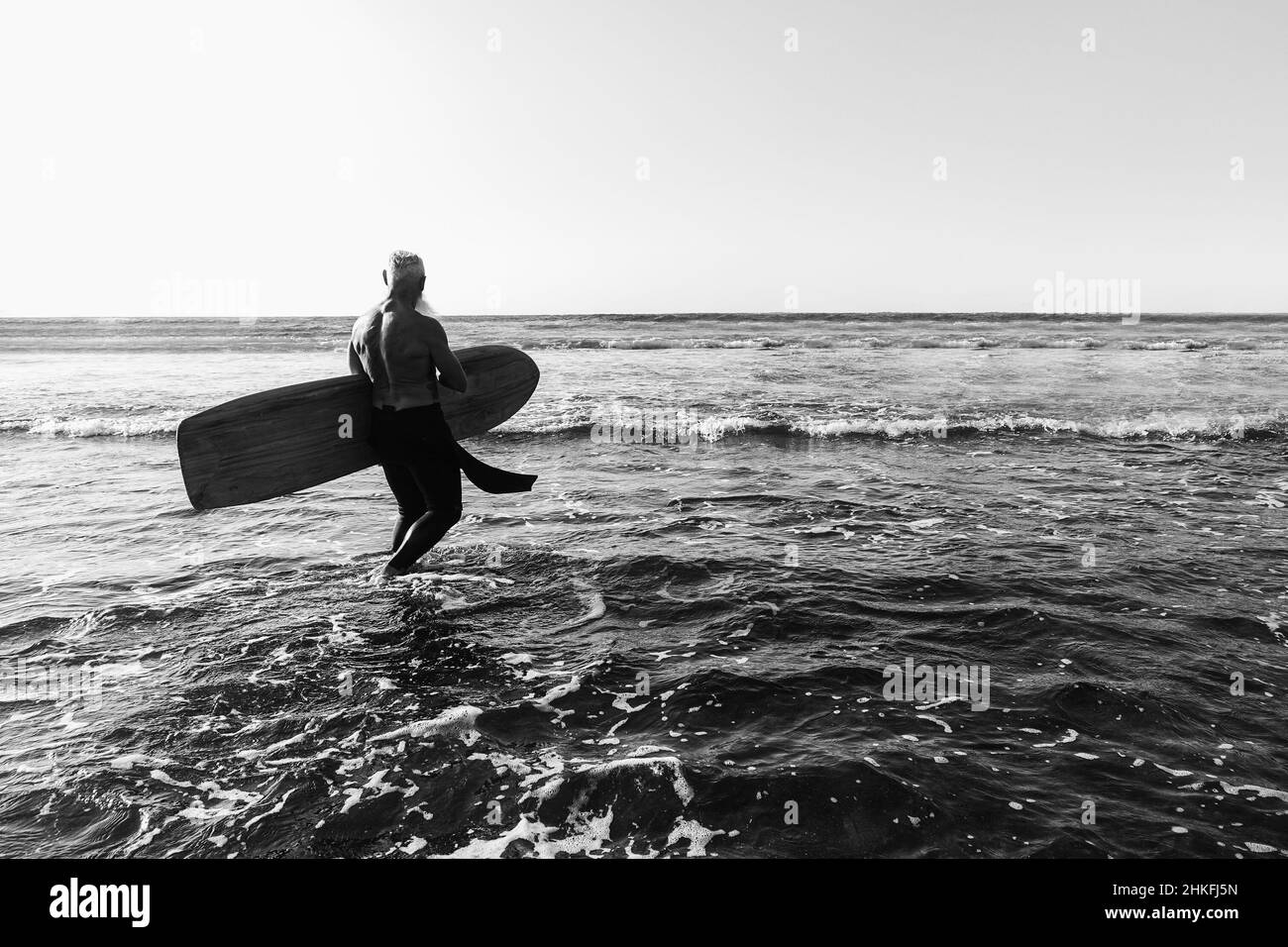 Black and White vintage style photo of a surfer entering the water to go surfing in Hawaii during sunset.