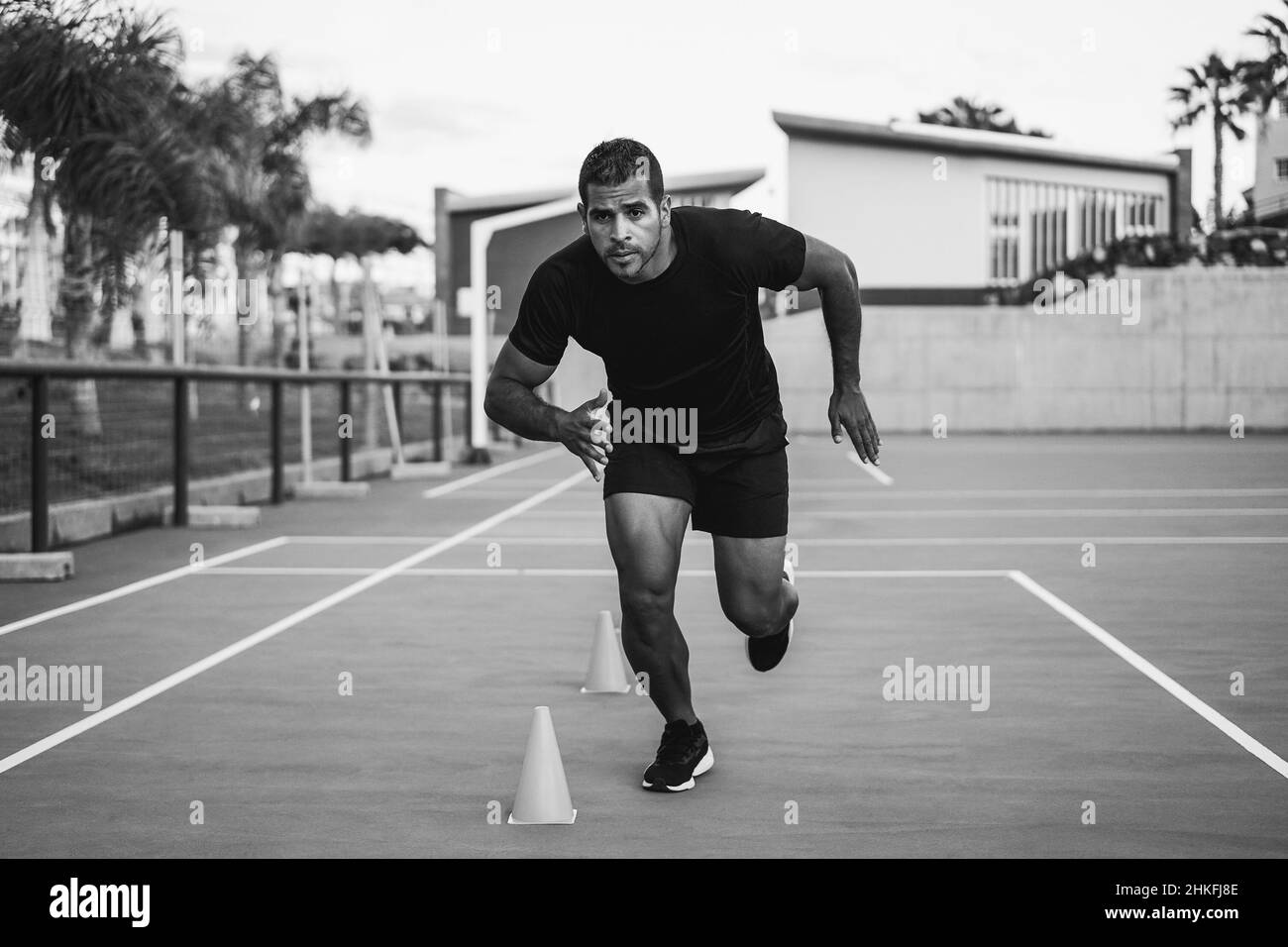 Hispanic man doing speed and agility cone drills workout session outdoors - Focus on man face - Black and white edition Stock Photo