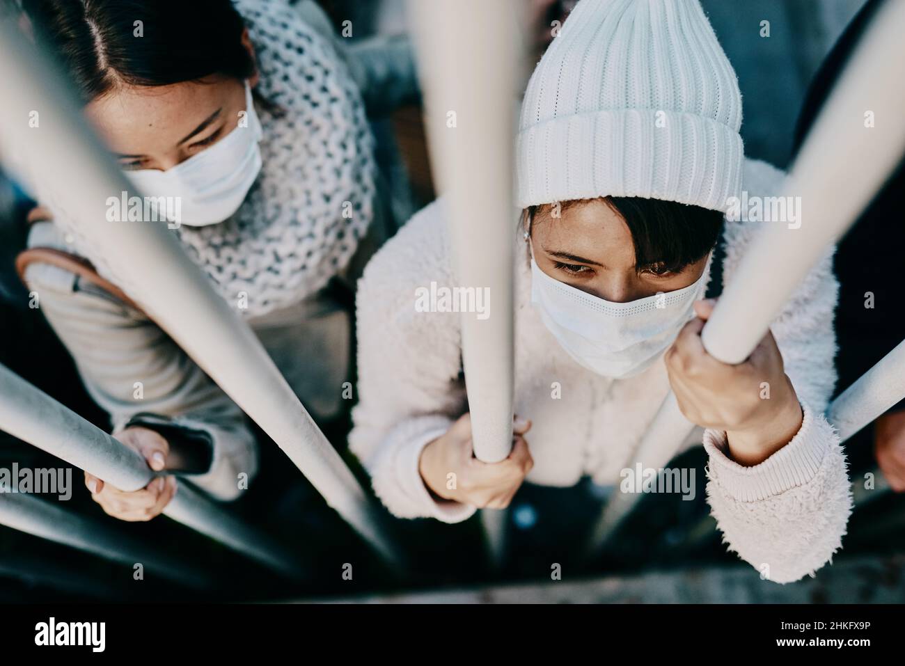 Prisoners of a viral war. Shot of a group of young people wearing masks while stuck behind a gate in a foreign city. Stock Photo