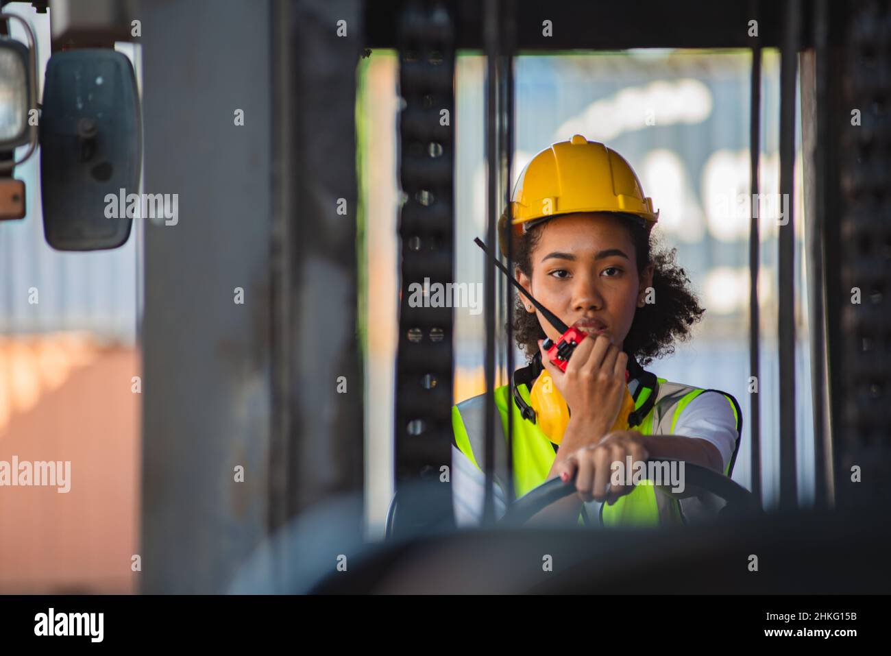 Female foreman use radio communication to communicate while driving forklift at shipping container yard. shipping in docks. Stock Photo