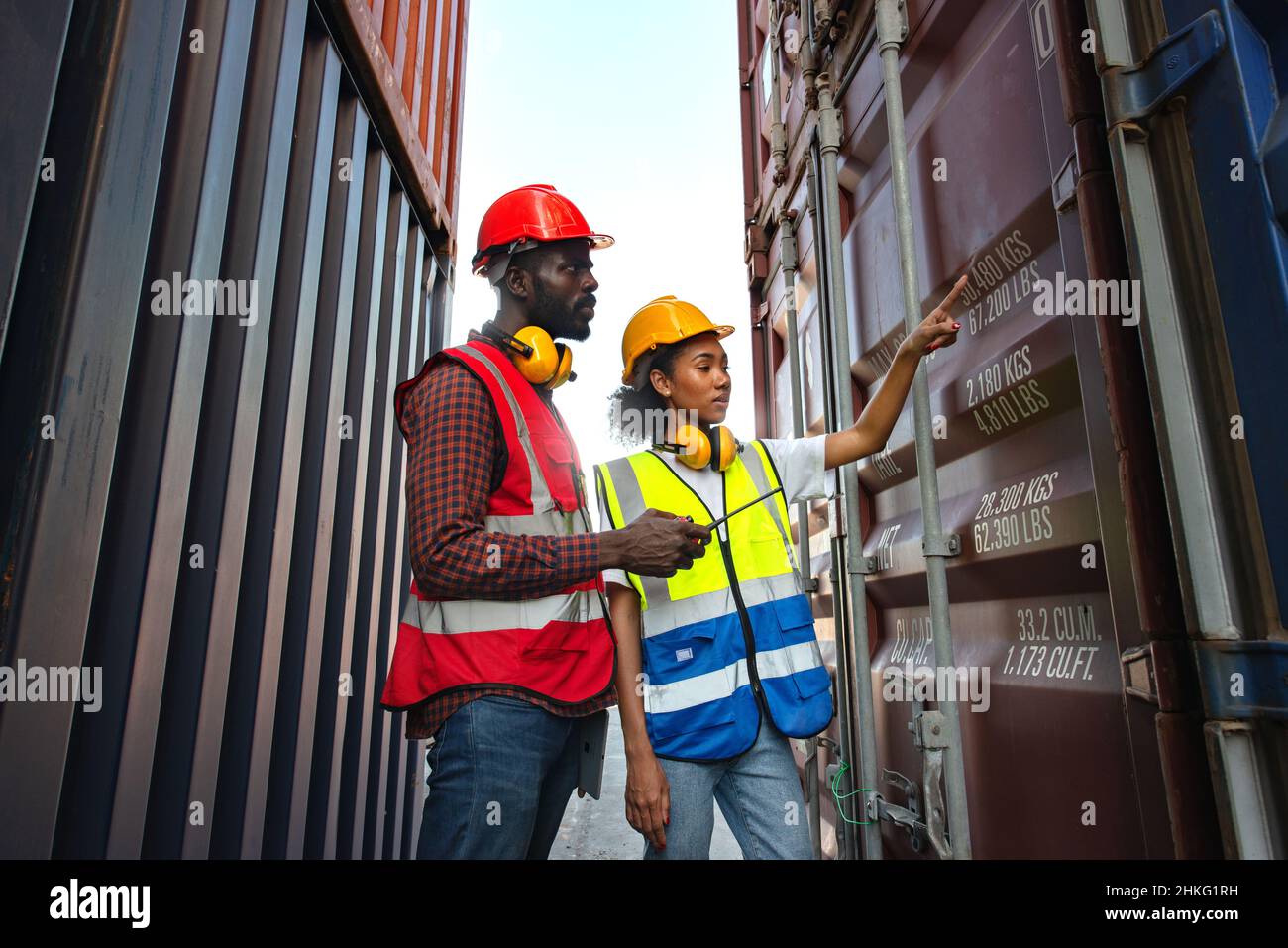 Two African american male and female worker check and control loading freight containers from Cargo freight ship for import export. Stock Photo