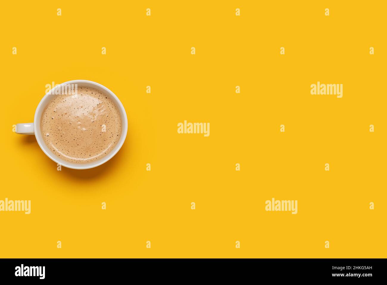 Cup of coffee in a white coffee cup mug with foam on a yellow