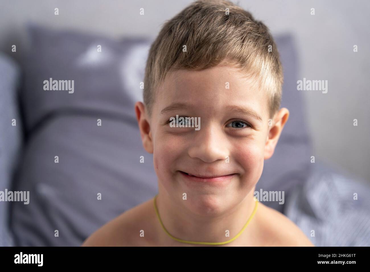 Portrait of a smiling cute Caucasian boy 5 years old who has just woken up and is sitting on the bed. Funny boy looks merrily at the camera Stock Photo