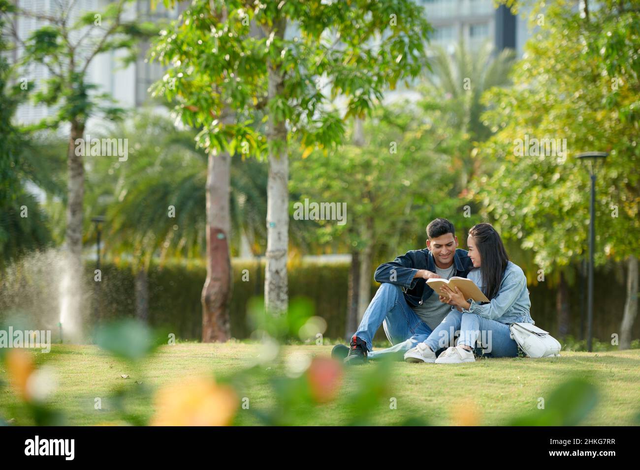 Young university students reading book for class together when sitting on grass on campus Stock Photo