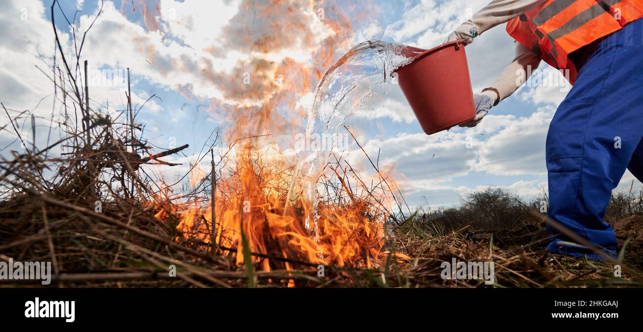Fireman ecologist extinguishing fire in field with cloudy sky on