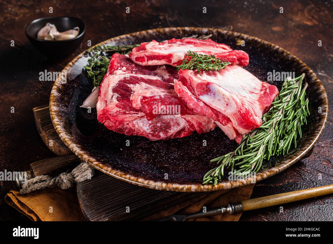 Uncooked Raw veal Short Ribs on rustic plate with rosemary. Dark background. Top view Stock