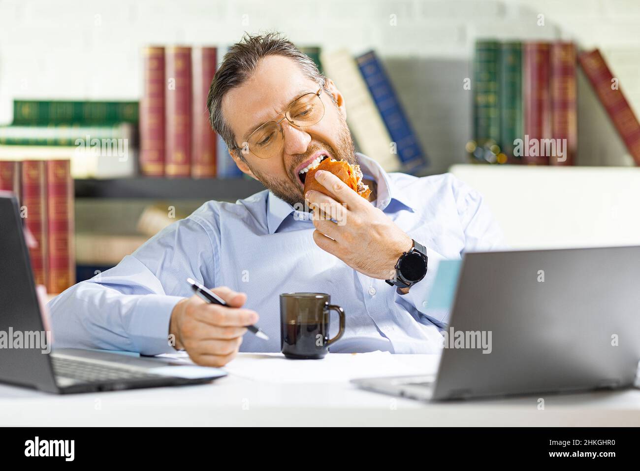 A middle-aged man is lounging in the office - he eats unhealthy food. Stock Photo