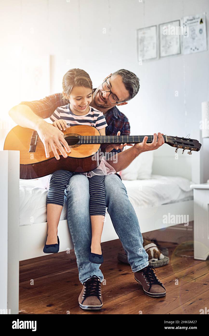 Teaching her about the different strings. Full length shot of a handsome mature man teaching his young daughter how to play the guitar. Stock Photo