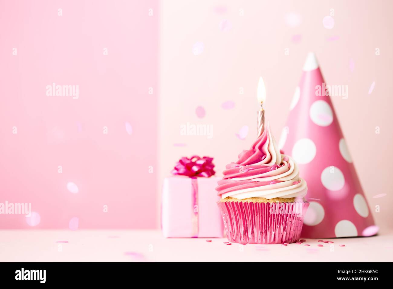 Pink birthday cupcake with candle, birthday gift and party hat Stock Photo