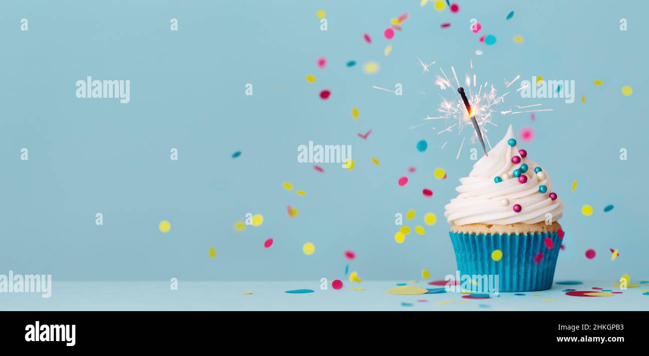 Birthday party background with birthday cupcake, celebration sparkler and colorful falling confetti Stock Photo