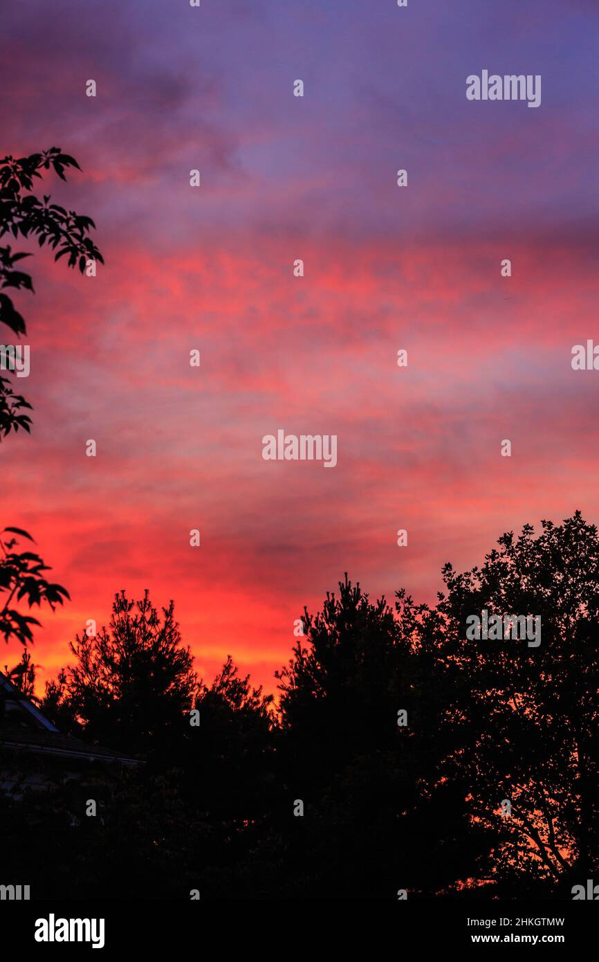 The first light of dawn glows bright reds, oranges and and blues painted on the passing clouds. Stock Photo