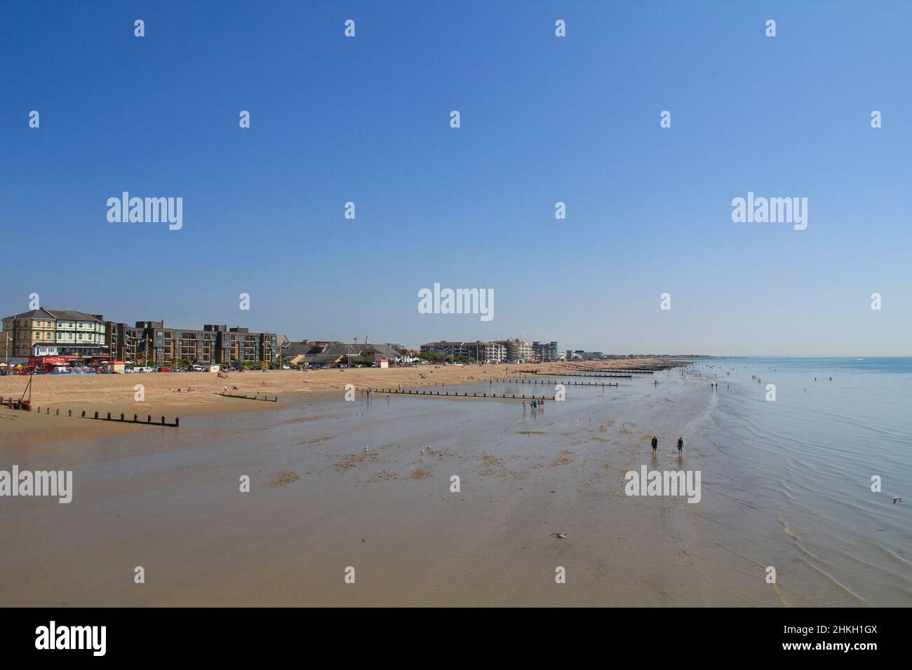Bognor Regis beach high up looking east from the pier at low tide with clear blue sky and expances of sand. Stock Photo