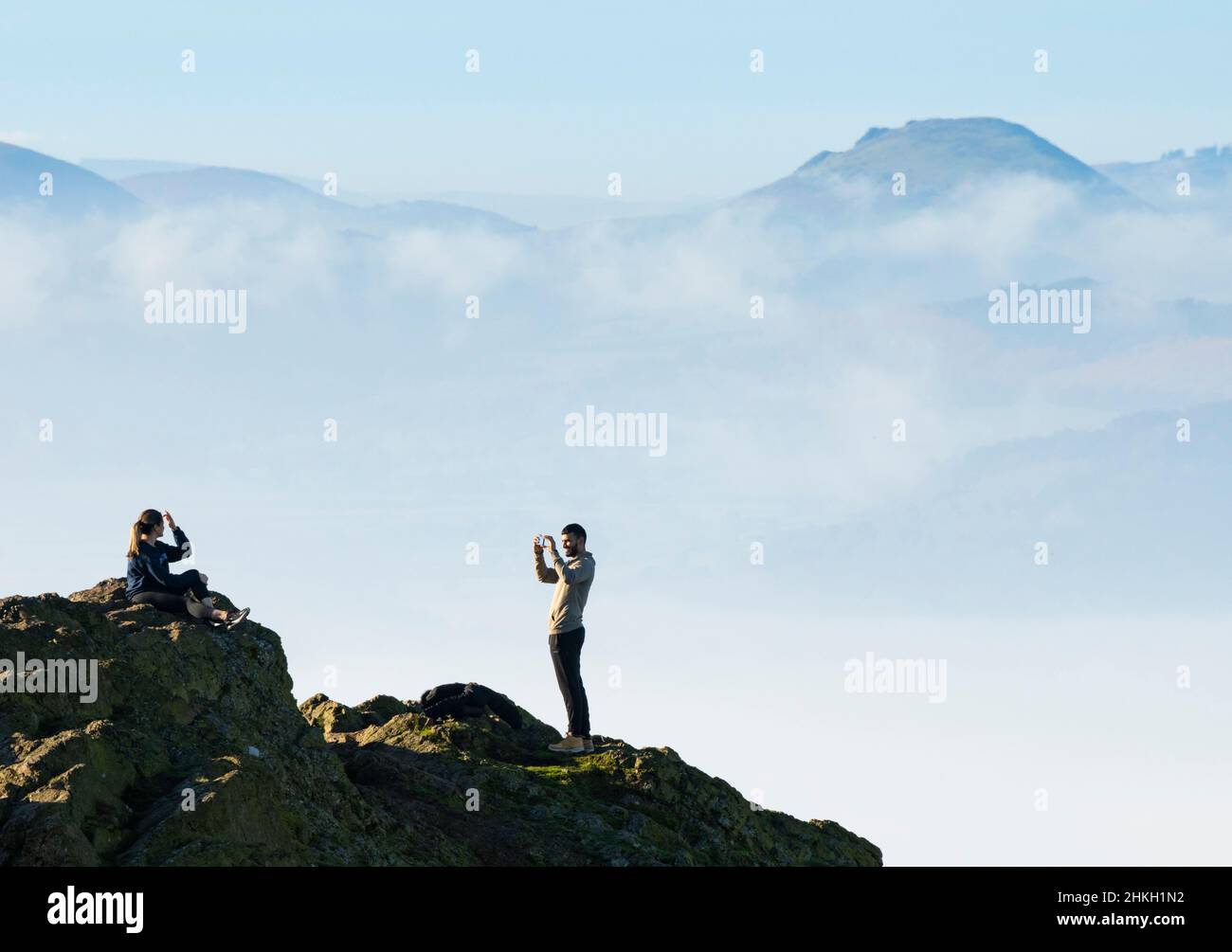A woman poses for a picture on the summit of the Wrekin, with Caer Caradoc and the Stretton Hills on the horizon, Shropshire. Stock Photo