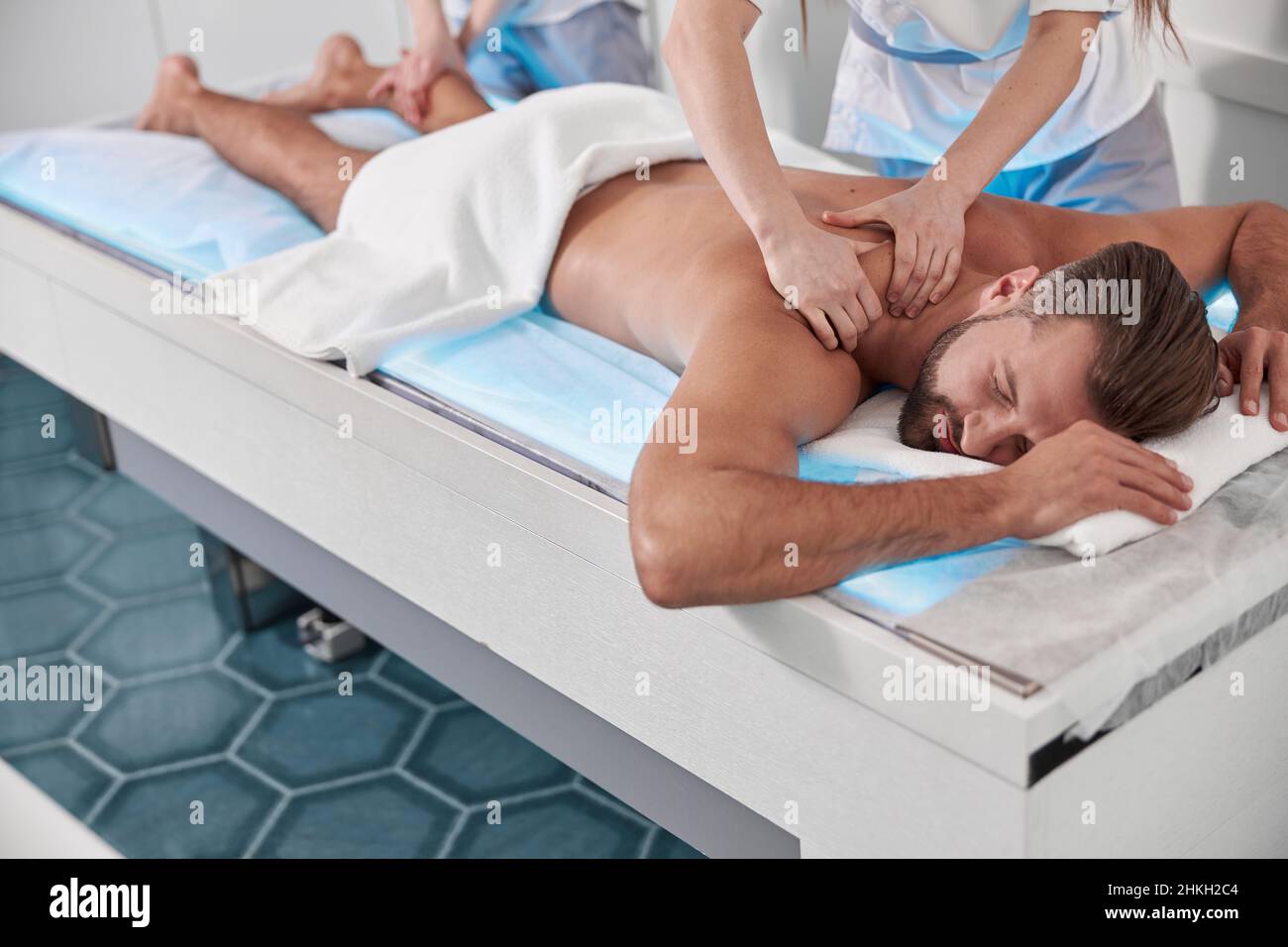 Careful doctor does massage of back to middle aged man with colleague in clinic Stock Photo