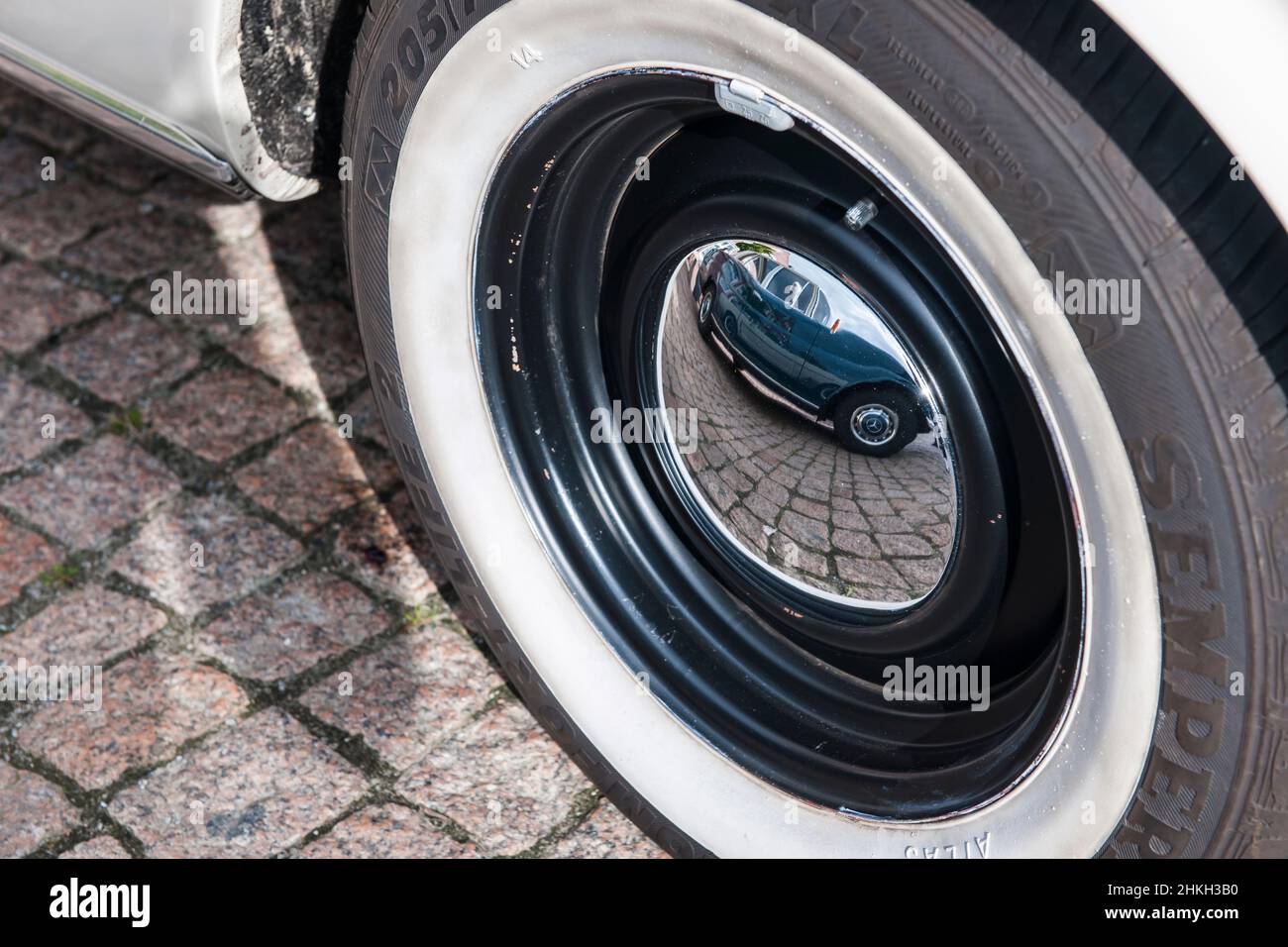 Close-up view of a vintage car tire with a chrome-plated hubcap and the mirror image of another German vintage car that can be seen in it. Stock Photo
