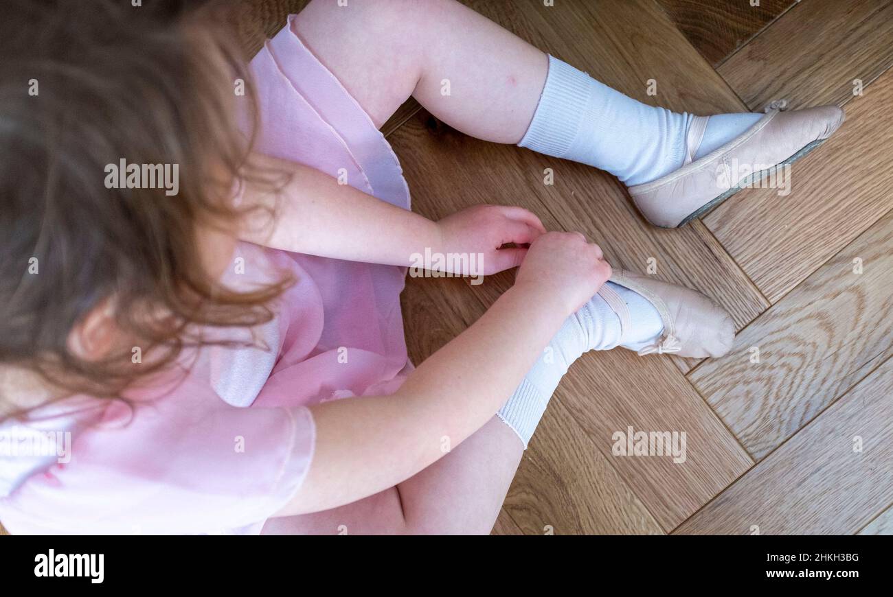 Cheeky young 5 year old girl putting on her ballet shoes ready for a dance class UK Stock Photo