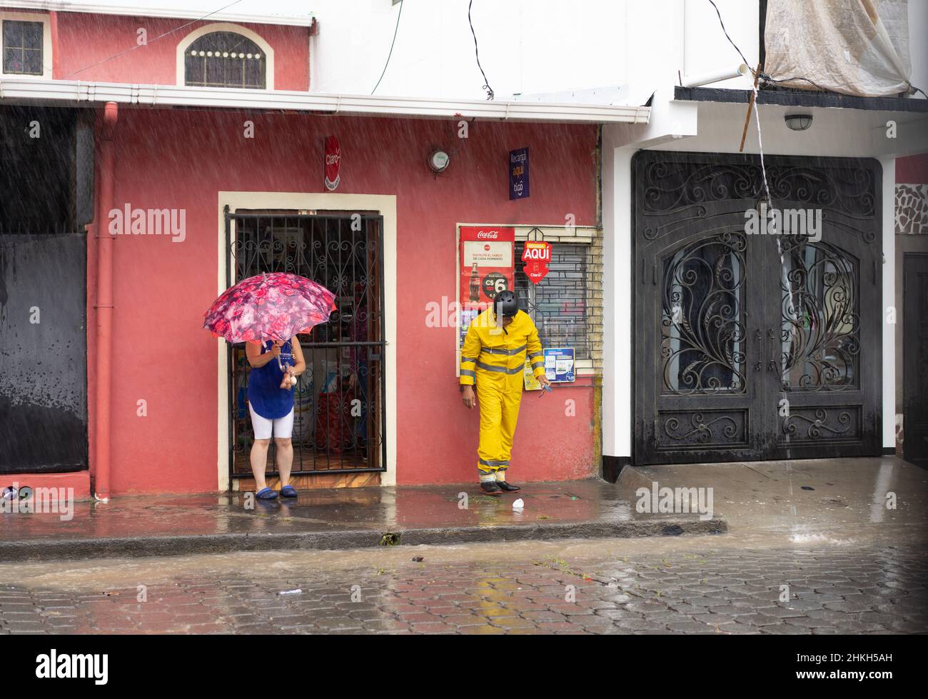 Two people wait under a roof overhand, hoping for a break in Hurricane Iota's rain in Jinotega, Nicaragua. Stock Photo