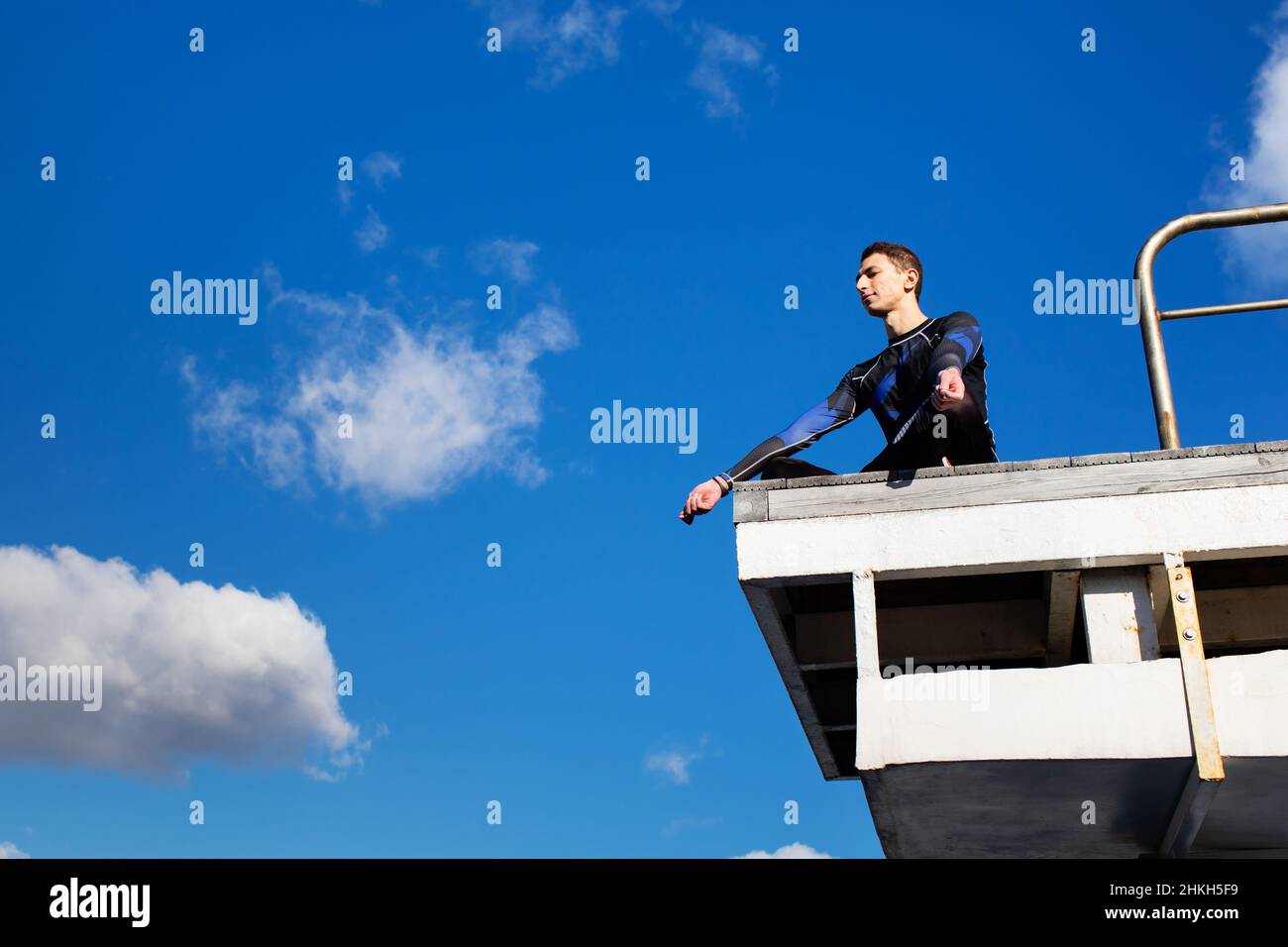 Swimmer in a swimming suit is sitting in the pool on a diving tower in the lotus position and resting Stock Photo