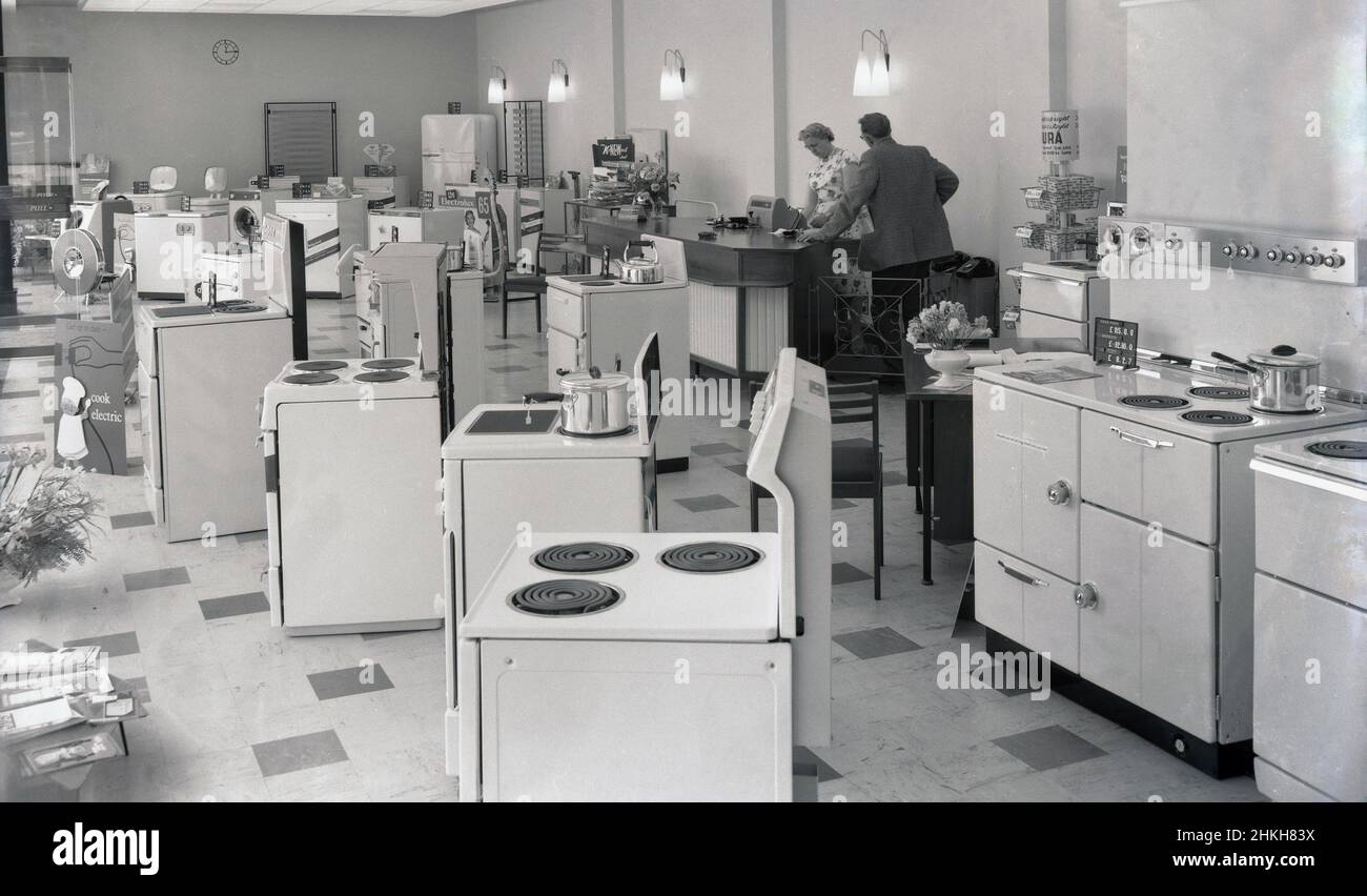 1960, historical, interior view of a new electrical appliance showroom and shop of Southern Electricity Services, Witney, Oxford, England, UK, showing the range of household appliances available, including the latest electric cookers. A promotional card on display, has the message 'get up todate, go electric'. A lady and gentleman stand at an area with a till. Brands of the day include Hotpoint, Kenwood and Electrolux. Stock Photo