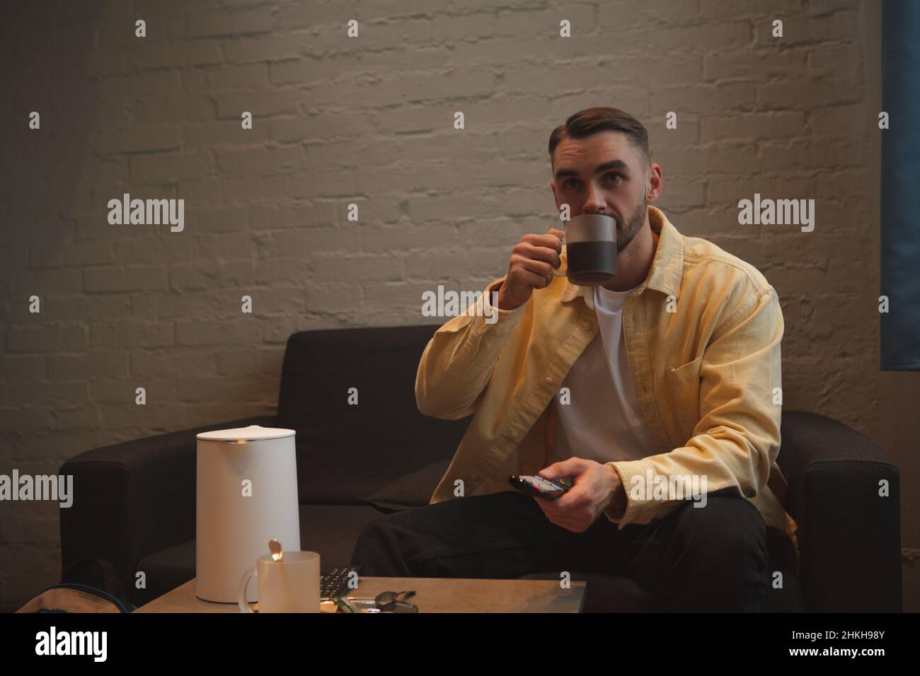 Handsome man watching tv while drinking coffee on a couch Stock Photo