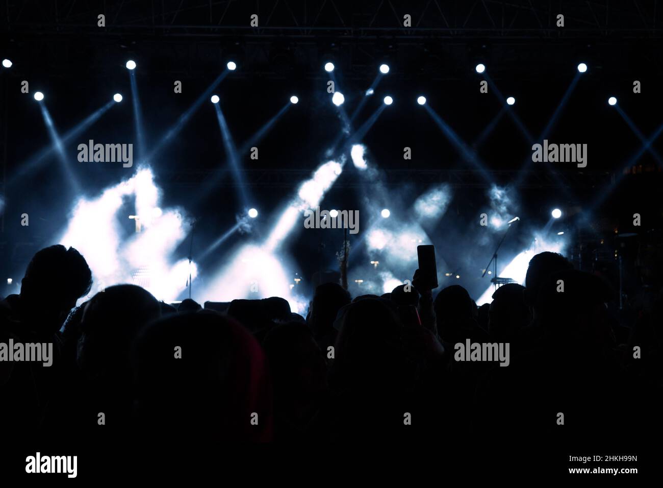 Spotlight on stage. Concert background with foggy effect on the stage. Silhouette of people. Noise included. Stock Photo