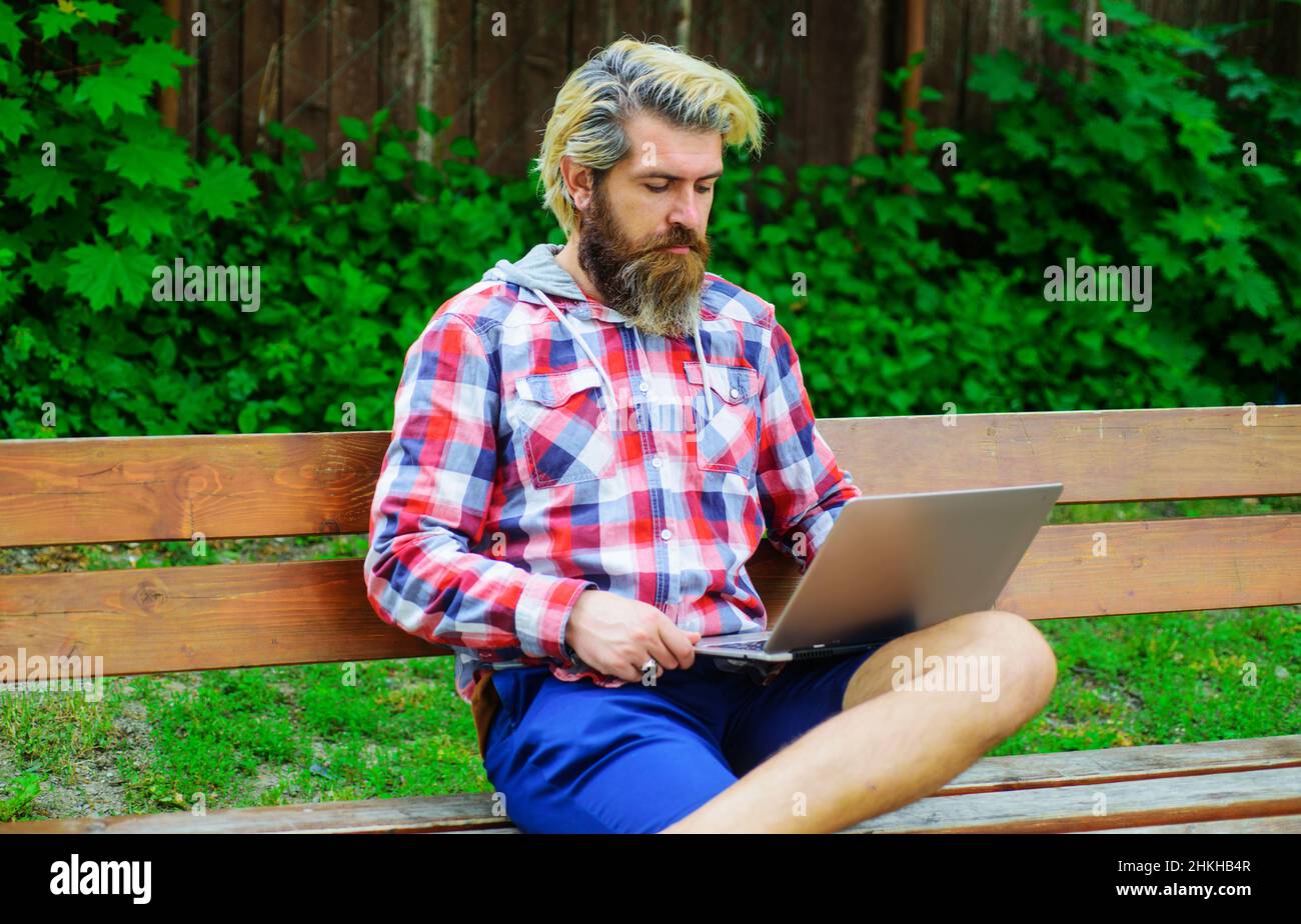 Bearded man with laptop working outdoors. Businessman with notebook in park. Study and work online. Stock Photo